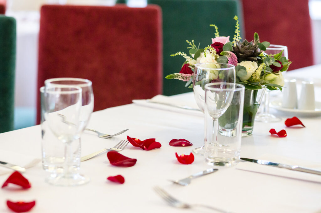 Rose petals on white linen table with glasses and cutlery.