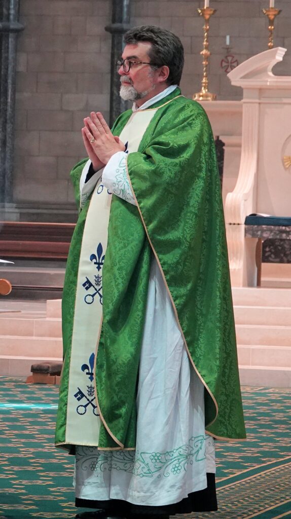 Father Alan Hodgson standing in green and white robes.